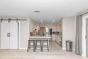 Una cocina moderna con una isla central, taburetes de bar y un armario con puerta corredera.