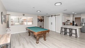 Une pièce spacieuse équipée d’une table de billard, d’un coin bar et offrant une vue sur l’extérieur.
