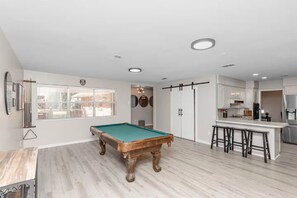 Una habitación amplia con mesa de billar, zona de bar y vistas al exterior.