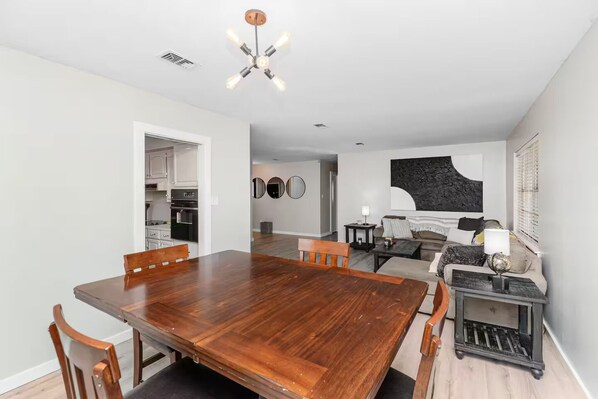 Un espacio habitable moderno con comedor, cocina y sala de estar con sofá y un cuadro abstracto grande.