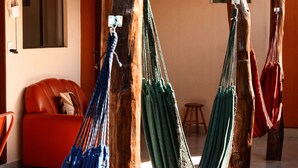 A room with a red sofa, wooden beams, and hammocks. - Pousada Árvore da Vida (Bonito)
