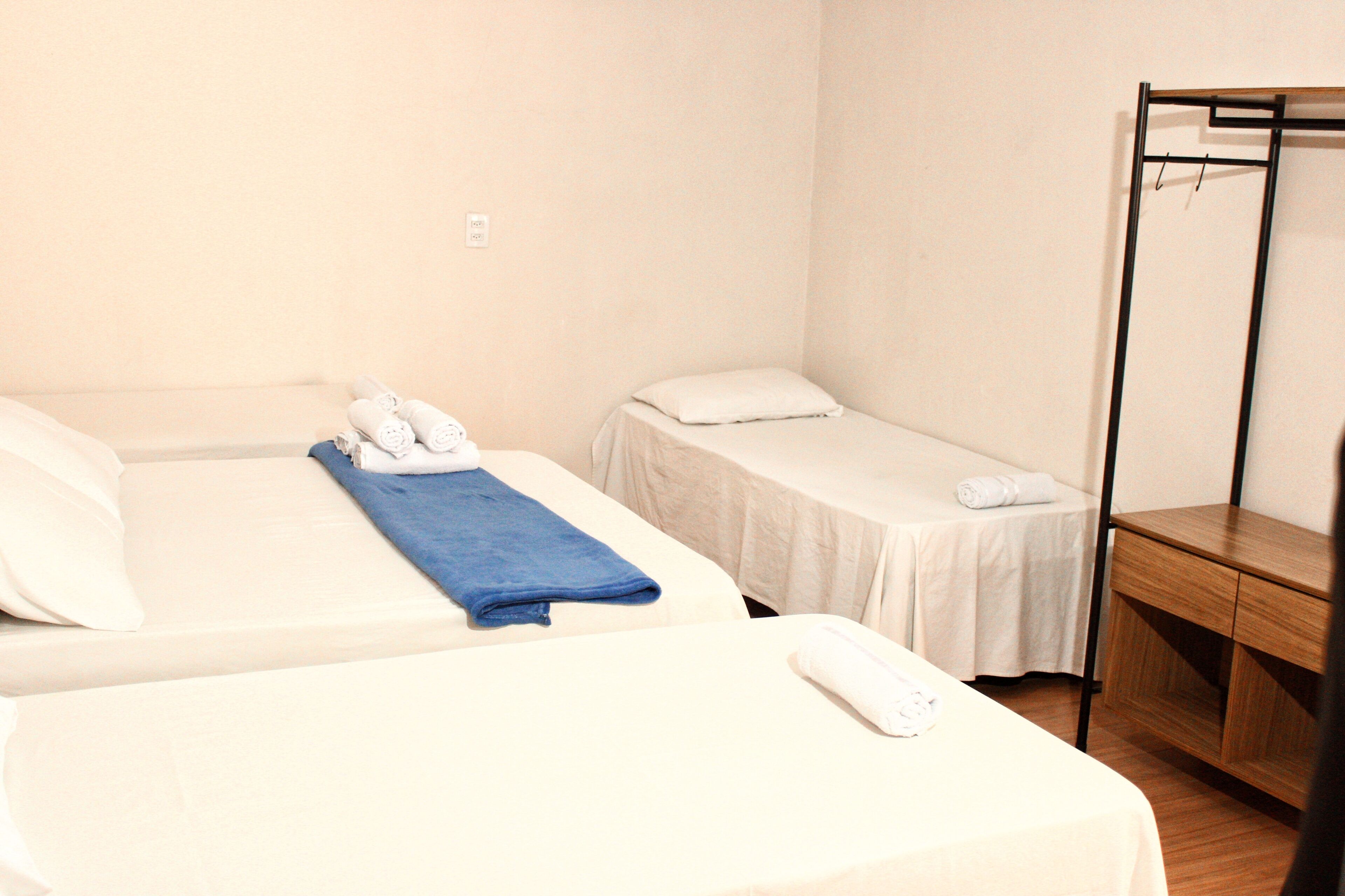 A hotel room with two beds, a wooden nightstand, and a metal rack.