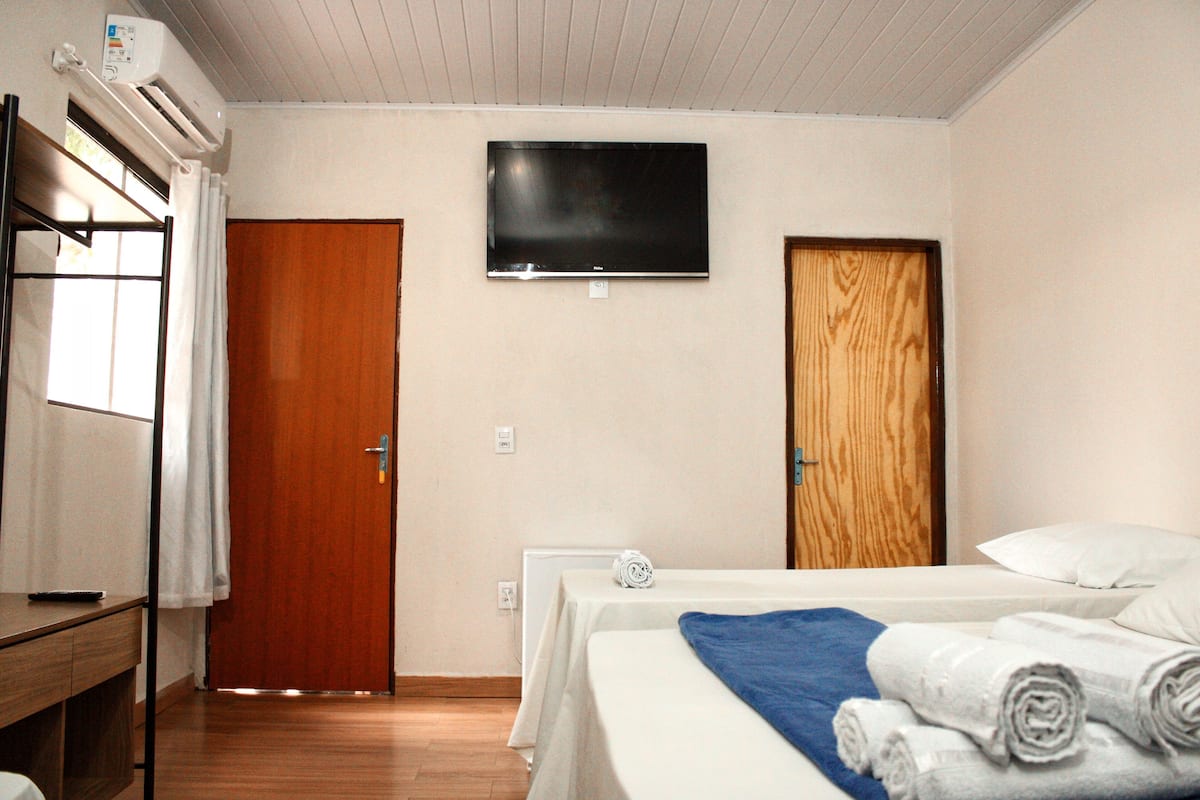 Ett hotellrum med en säng, en TV, ett skrivbord och ett fönster med gardiner.