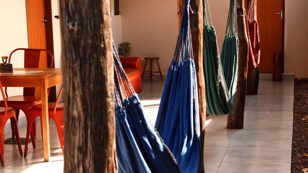 A room with a wooden table, red chairs, and blue hammocks hanging from wooden posts. - Pousada Árvore da Vida (Bonito)