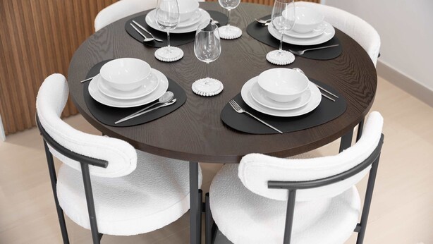 Una mesa redonda con sillas blancas, dispuesta con platos, vasos y cubiertos.