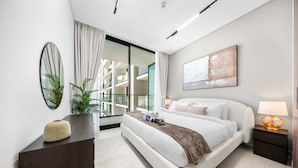 Una habitación de hotel moderna con una cama grande, una mesita de noche con lámpara, una planta en maceta y vistas a la ciudad a través de un ventanal amplio.