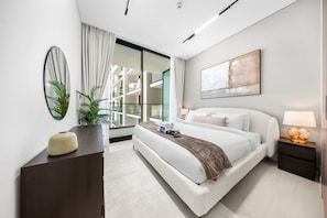 Une chambre d’hôtel moderne avec un grand lit, une table de chevet avec une lampe, une plante en pot et une vue sur la ville par une grande fenêtre.