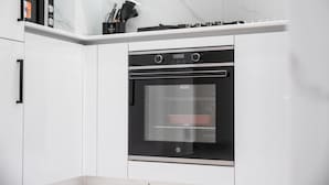 Una cocina moderna con horno empotrado, armarios blancos y una salpicadera de mármol.