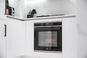 Une cuisine moderne dotée d’un four encastré, de meubles blancs et d’un dosseret en marbre.