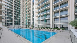 Un hotel moderno con piscina, varios balcones y sillones de descanso.