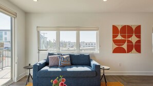 Ein modernes Wohnzimmer mit einem blauen Sofa, einem großen Fenster und einem geometrischen Kunstwerk an der Wand.