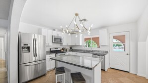 A modern kitchen with stainless steel appliances, a central island with stools, and a view of the outdoors.