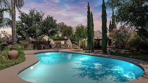 A swimming pool surrounded by trees and a patio area with outdoor furniture.