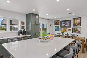 Une cuisine moderne dotée d’un grand îlot central, d’un coin repas avec une table pour quatre personnes et d’une vue sur le jardin arrière.