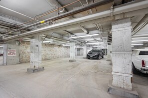 A parking garage with concrete pillars, a caution sign, and a black SUV parked. - Open-Concept Loft Exchange District | 1 Bed | 1 Bath | (Winnipeg)
