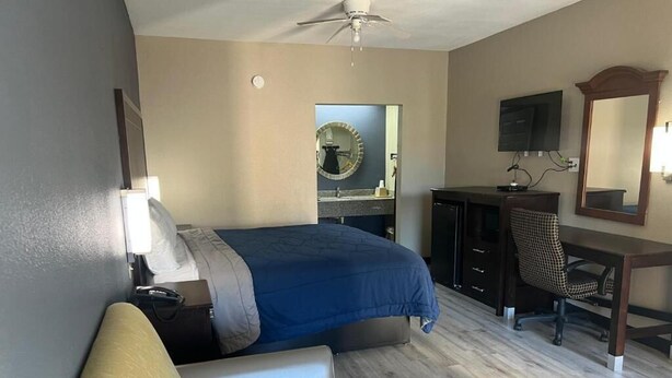 Un dormitorio con cama, escritorio, silla, espejo y ventilador de techo.