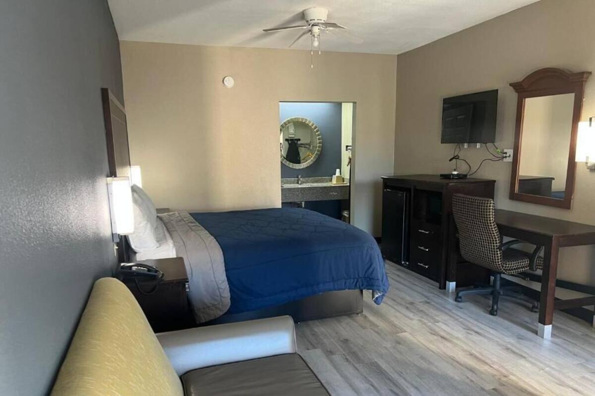 A bedroom with a bed, a desk, a chair, a mirror, and a ceiling fan.