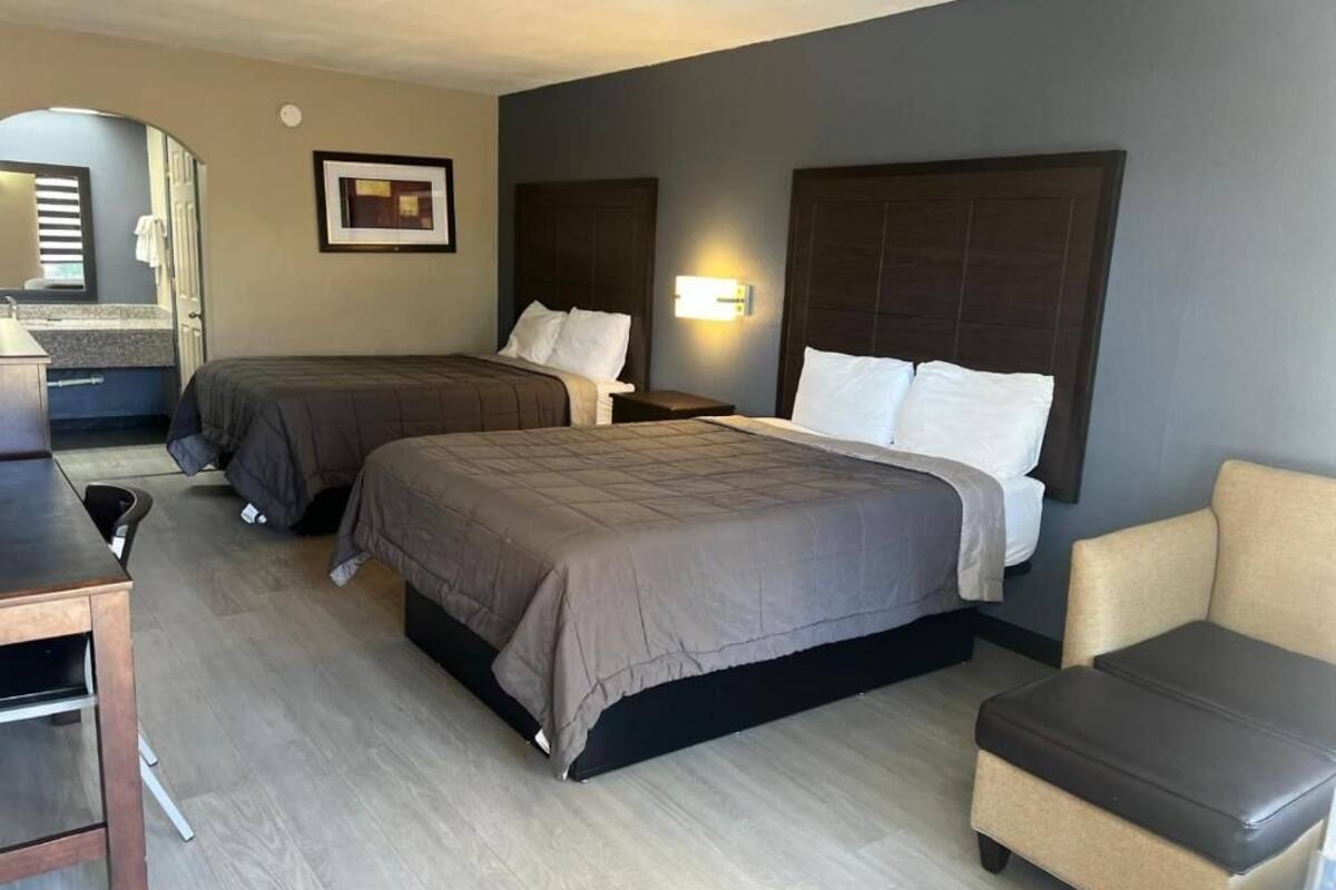 A hotel room with two beds, a desk, a chair, and a small table.
