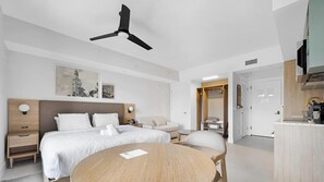 Una camera d'hotel moderna con un letto, comodini, un tavolino rotondo, una sedia, una ventola a soffitto, opere d'arte al muro e un angolo cottura.