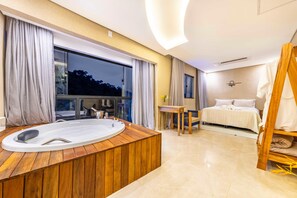 A modern hotel room with a wooden bathtub, a bed with white bedding, a small table, and a view of the outdoors. - Casa Happiness Paraty | Boat tour included (Paraty)