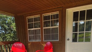 A wooden porch with two red chairs and a white door. - Cozy Two Loft Tiny House Cabin near beautiful Roaring River with AC (Cassville)