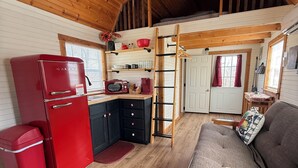 A compact kitchen with a refrigerator, microwave, and wooden shelves. - Cozy Two Loft Tiny House Cabin near beautiful Roaring River with AC (Cassville)
