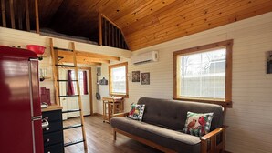 A wooden interior with a sofa, a red refrigerator, a ceiling fan, and a window with blinds. - Cozy Two Loft Tiny House Cabin near beautiful Roaring River with AC (Cassville)