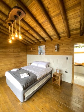 A wooden cabin-style bedroom with a bed, bedside table, and a hanging light fixture. - Family cabin with private pool, panoramic view. (Nocaima)
