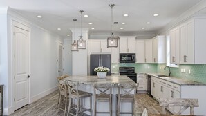 A kitchen with white cabinets, a marble countertop, and a central island with bar stools. - Destiny Awaits | 6BR | Gulf View! Private Pool & Golf Cart! Walk to Beach! (Destin)