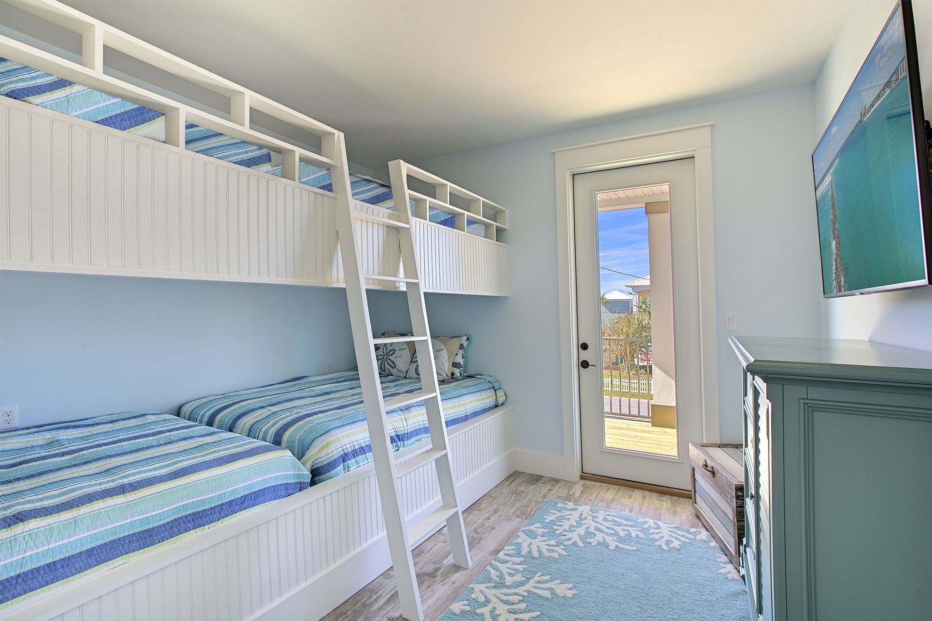 A room with bunk beds, a ladder, a door leading outside, and a TV on the wall.