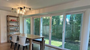 A dining area with a wooden table and chairs, a bookshelf, and a sliding glass door leading to a backyard.