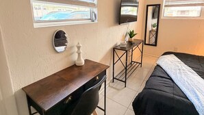 Ein Schlafzimmer mit einem Bett, einem Schreibtisch mit Stuhl, einem Fernseher und zwei Fenstern mit Jalousien.