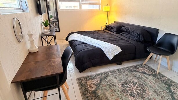 Ein Schlafzimmer mit Bett, Schreibtisch, Stuhl, Lampe und Teppich.