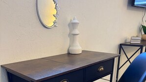 Ein Schreibtisch mit zwei Schubladen, ein Stuhl, ein Spiegel und eine kleine weiße Vase auf einer dunklen Holzschreibtischplatte vor einer weißen Wand.
