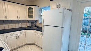 Una cocina con armarios blancos, encimera negra, refrigerador blanco y ventilador de techo.