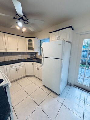 A kitchen with white cabinets, a black countertop, a white refrigerator, and a ceiling fan. - Quiet Home Near Wilton Dr | Sleeps 6 |10 Min Beach (Wilton Manors)