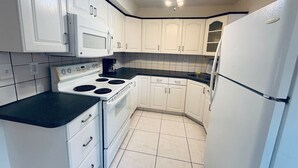 Una cocina compacta con armarios blancos, estufa, microondas y refrigerador.