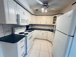A compact kitchen with white cabinets, a stove, a microwave, and a refrigerator. - Quiet Home Near Wilton Dr | Sleeps 6 |10 Min Beach (Wilton Manors)