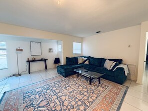 Ein Wohnzimmer mit einem Ecksofa, einem Couchtisch, einem gemusterten Teppich, einem Beistelltisch und einer Lampe.