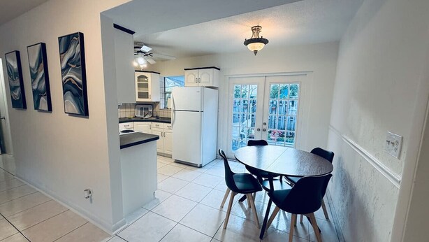 Una cocina moderna con armarios blancos, una mesa de comedor con sillas y vistas al exterior a través de una ventana.