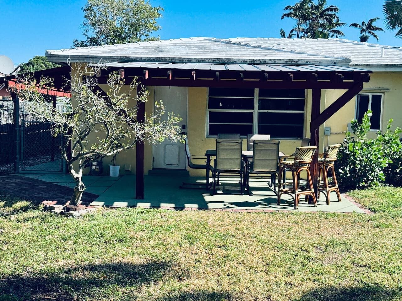 Uma casa com varanda coberta, área de estar externa e uma pequena árvore.