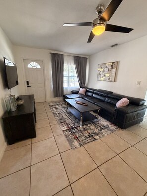A living room with a sofa, coffee table, TV, and ceiling fan. - Fort Lauderdale Gem Private Yard and Patio (Fort Lauderdale)