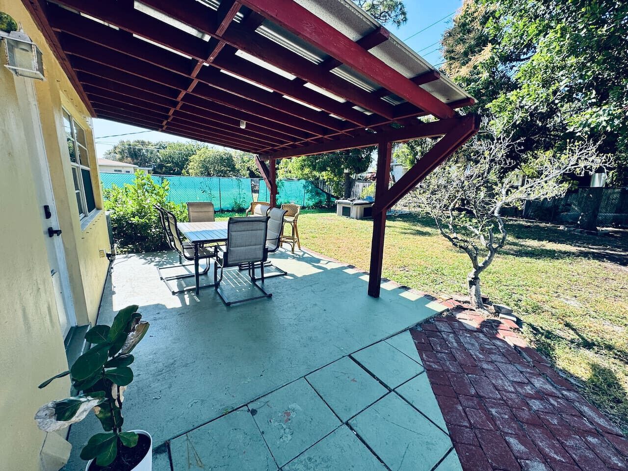A covered patio area with a table and chairs, a small tree, and a brick pathway.