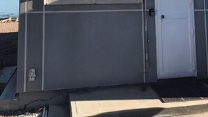 A small building with a white awning over a window, a door, and a metal vent on the roof.