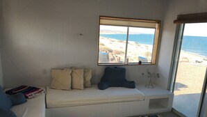 A room with a bench, pillows, a striped rug, and a window with a beach view.