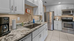 Una cocina con armarios blancos, electrodomésticos de acero inoxidable, encimera de mármol y un reloj en la pared.