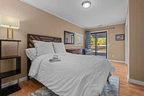 A bedroom with a bed, bedside table, lamp, and a view through a glass door. - Windmere Cottage in Charming Pinehurst (Pinehurst)