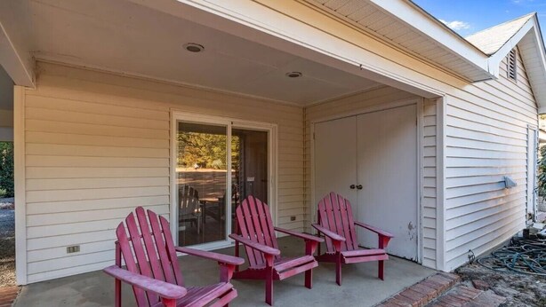 Una casa con porche cubierto, tres sillas Adirondack y un ventanal corredero.