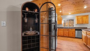 A kitchen with wooden cabinets, a black wine rack, and a glass door partition. - Pine Cottage (Big Bear Lake)