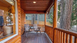A wooden deck with a railing, a table, and chairs. - Pine Cottage (Big Bear Lake)